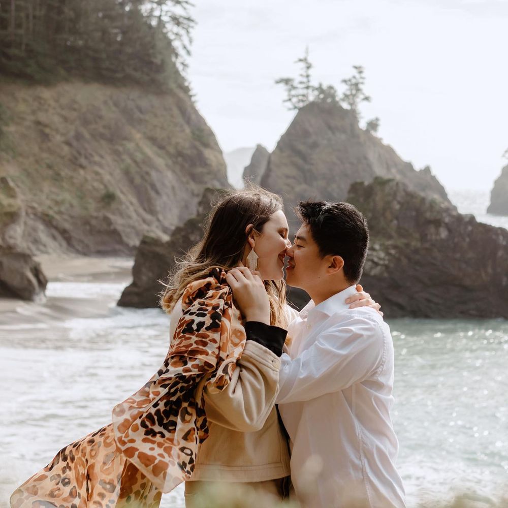 Engagement photo of Jess and her husband kissing by the ocean with cliffs in the background