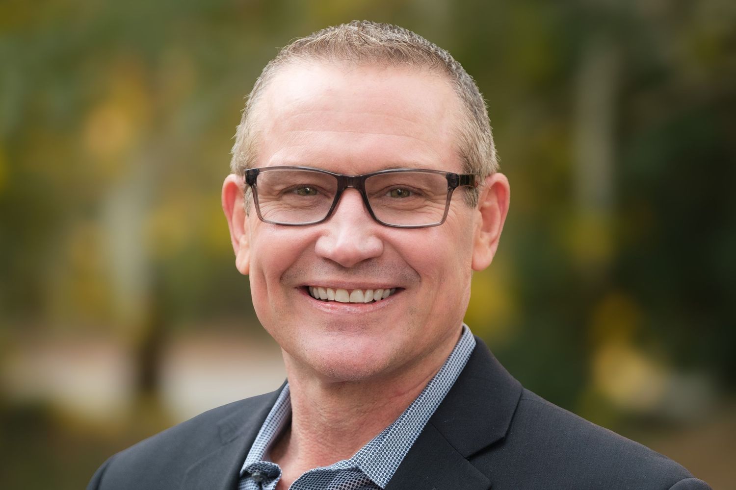 A smiling business professional with glasses and a blue suit.