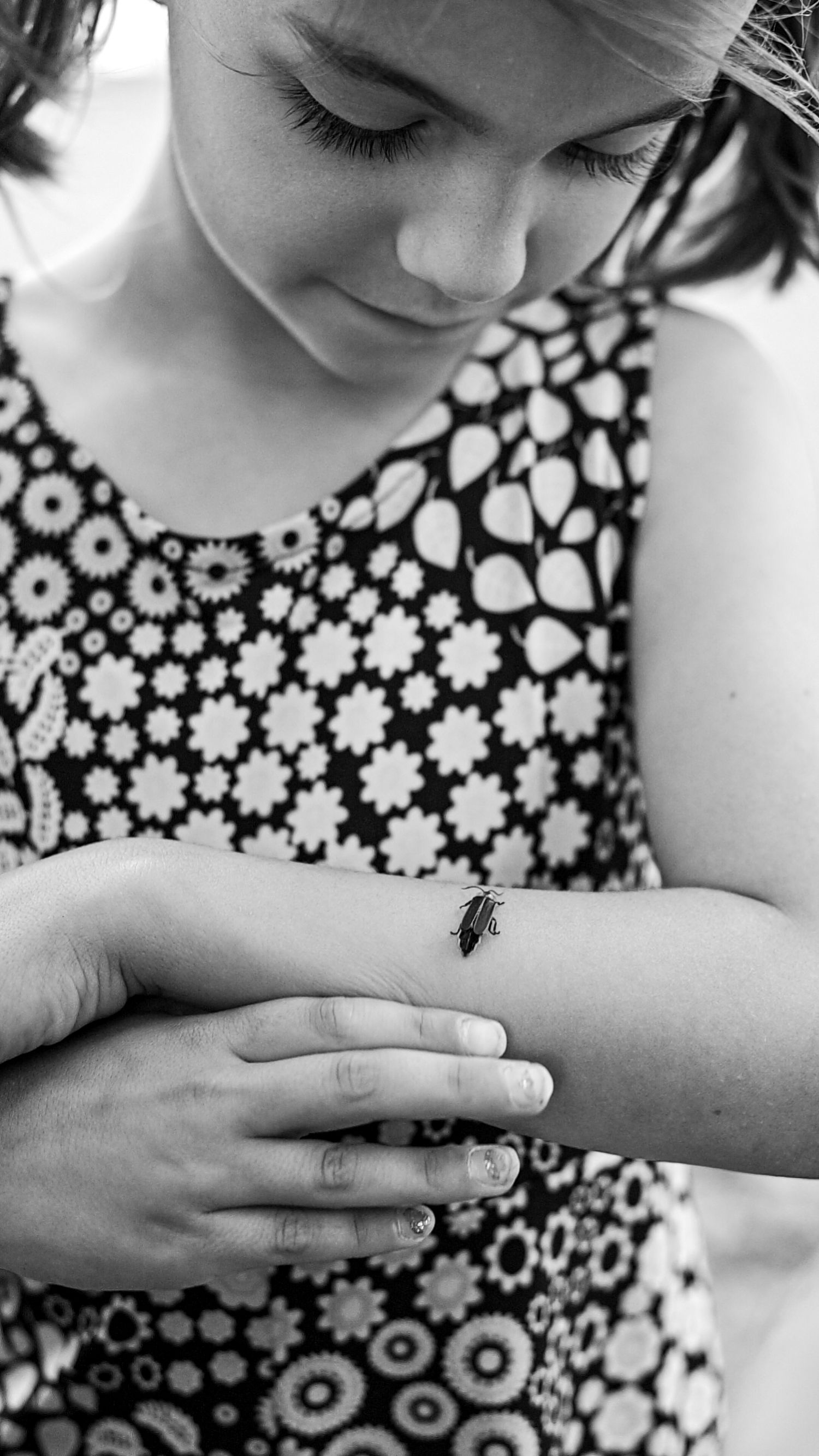 Close-up of someone wearing floral dress examining small insect on their arm in monochrome.