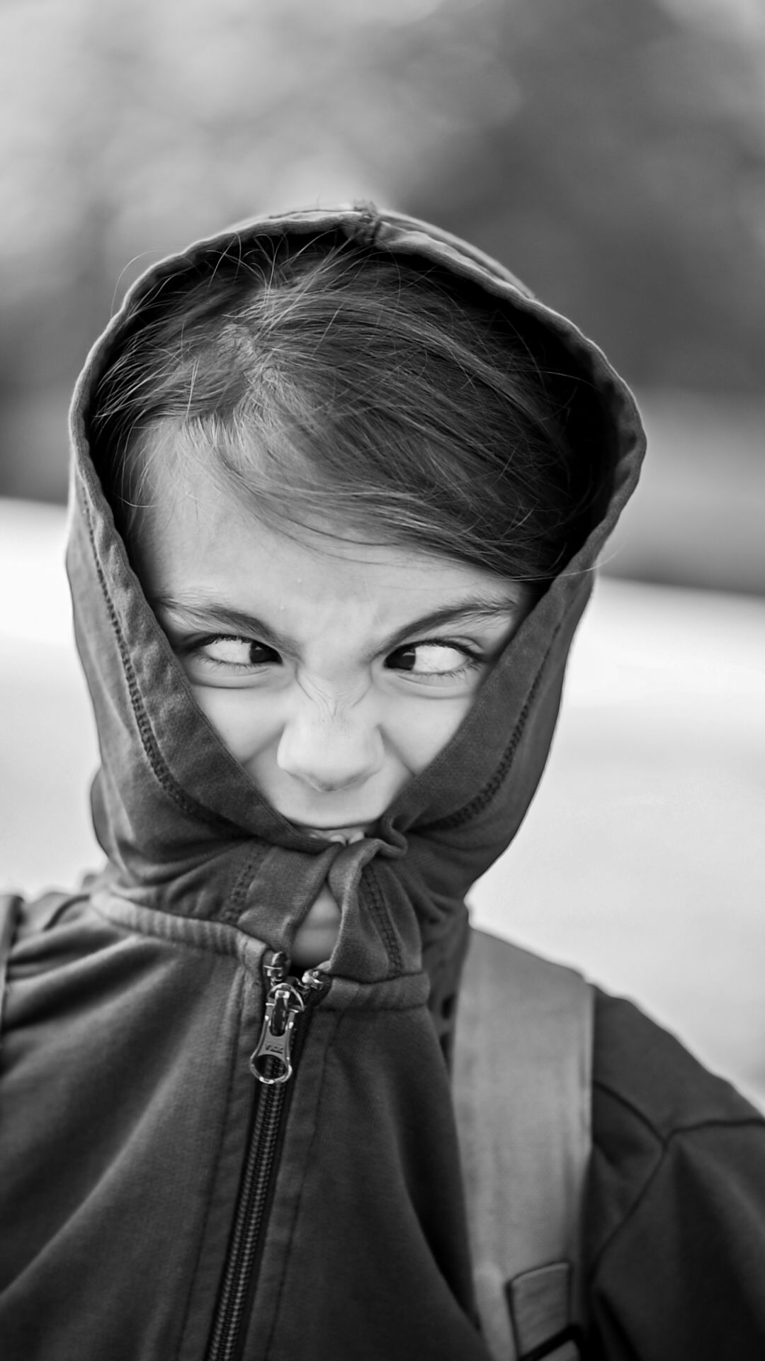 Figure in hooded jacket looking sideways with playful expression in black and white portrait.