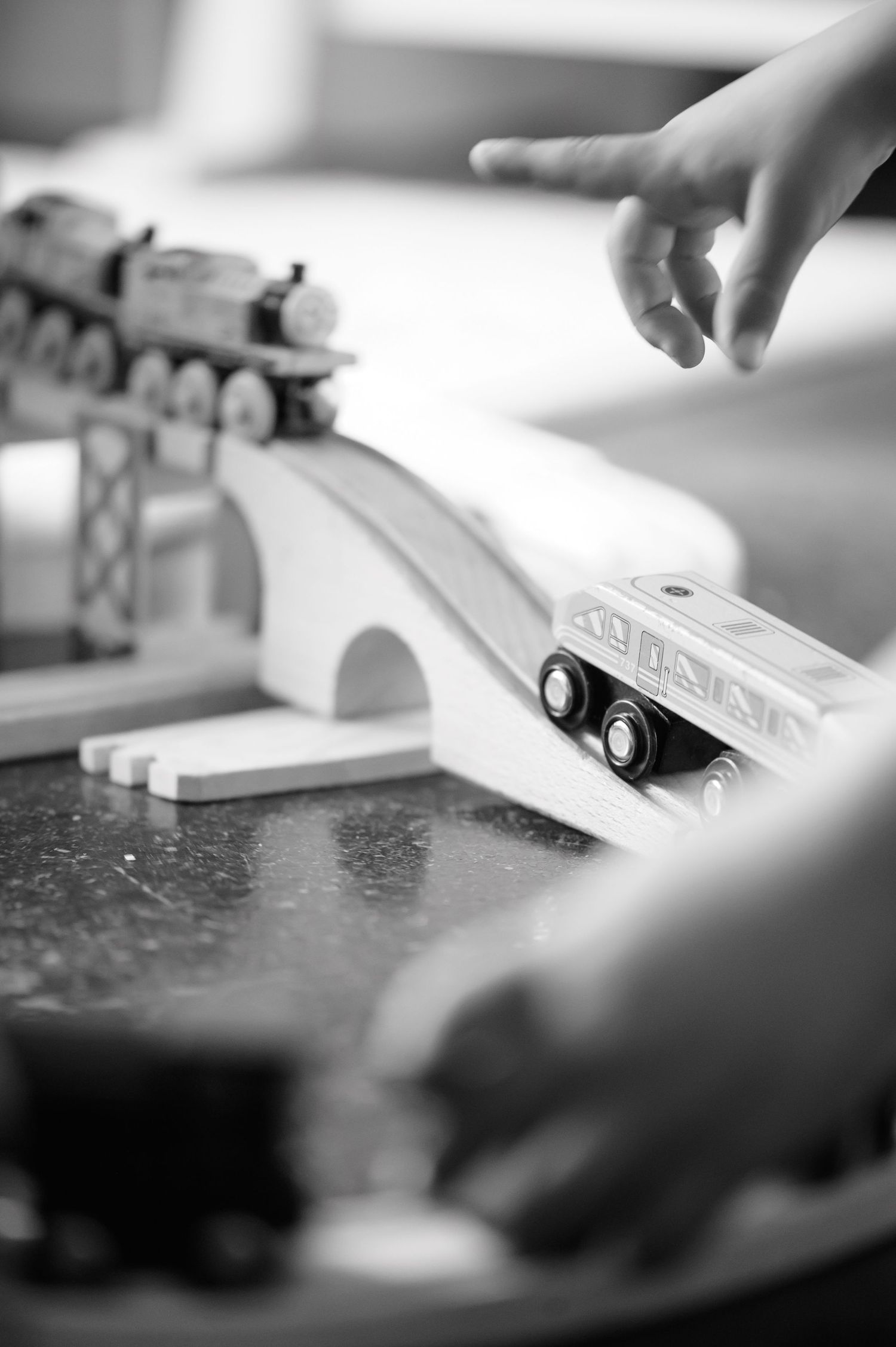 Close-up of toy trains on a bridge track set, photographed in black and white.