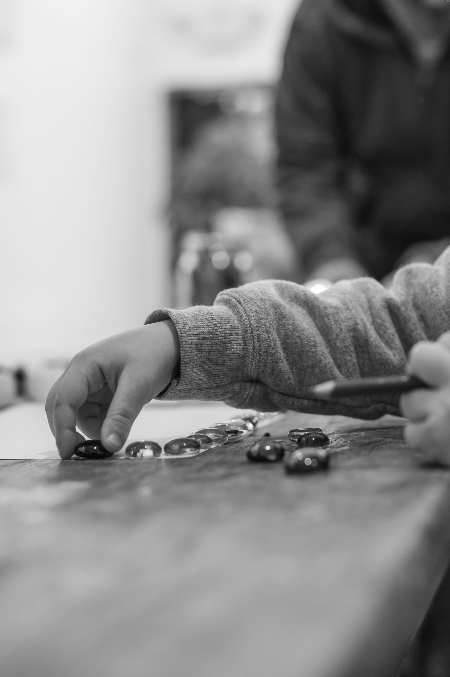 Black and white photo of hands playing with toy cars on a flat surface.