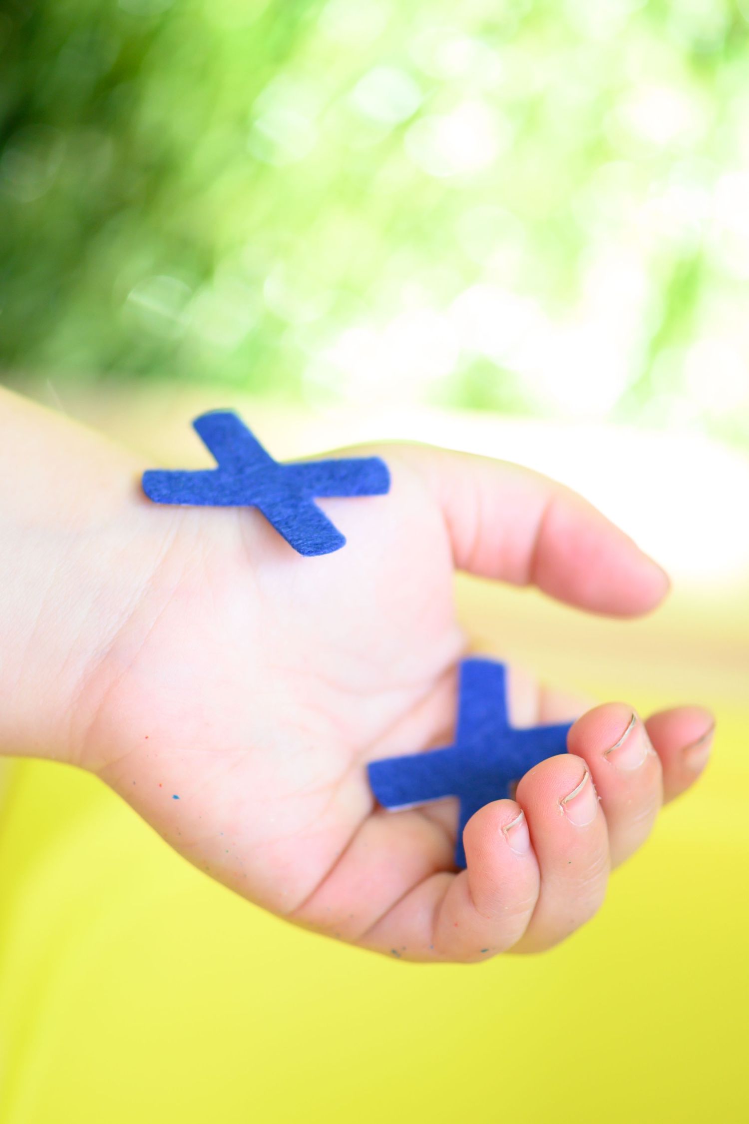 Two small blue cross-shaped objects held in an open palm against a blurred green background.