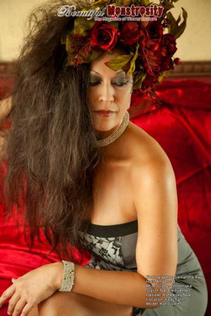 Glamour photo with floral headpiece against red backdrop featuring dramatic makeup and jewelry.