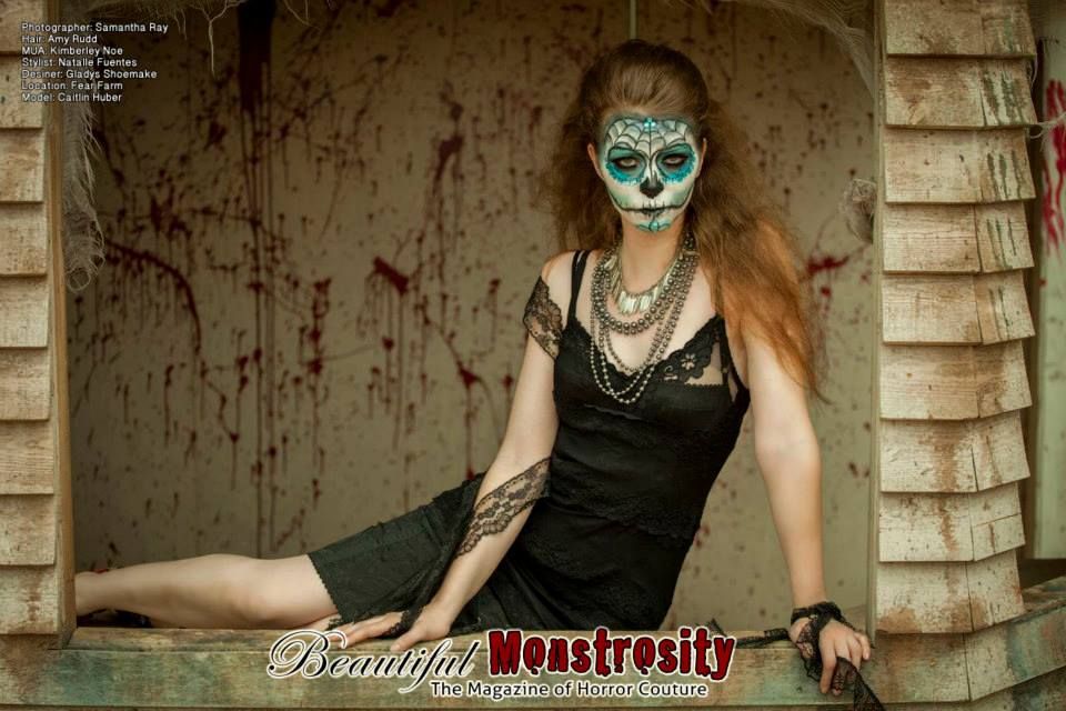 Gothic themed portrait with turquoise face paint and black dress against weathered wall.