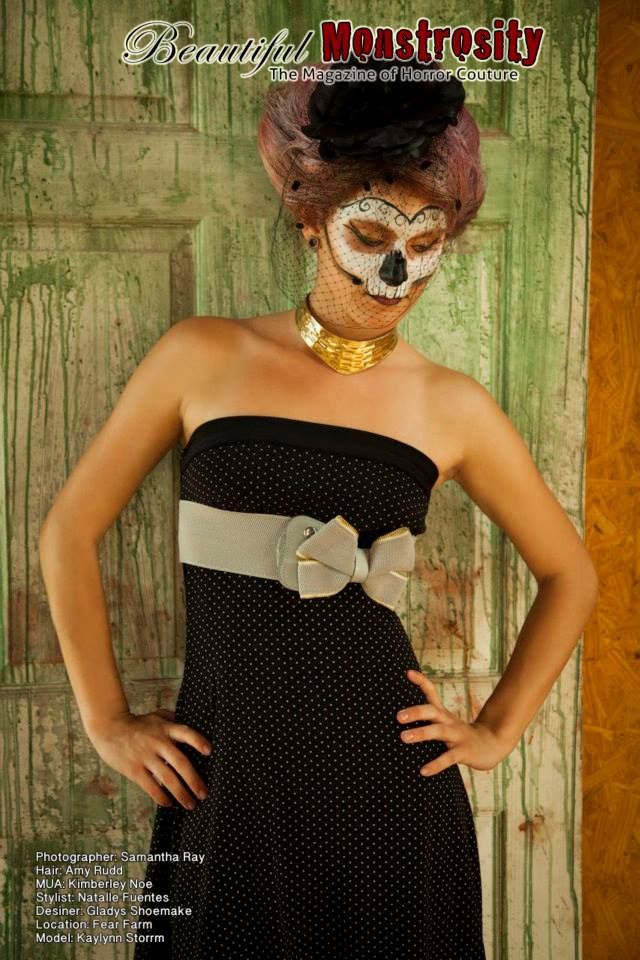Model in polka dot dress with sugar skull makeup and vintage hairstyle against green wall.