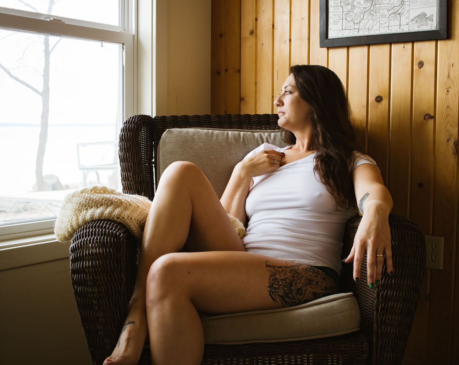 Person relaxes in wicker chair by window in casual tank top.