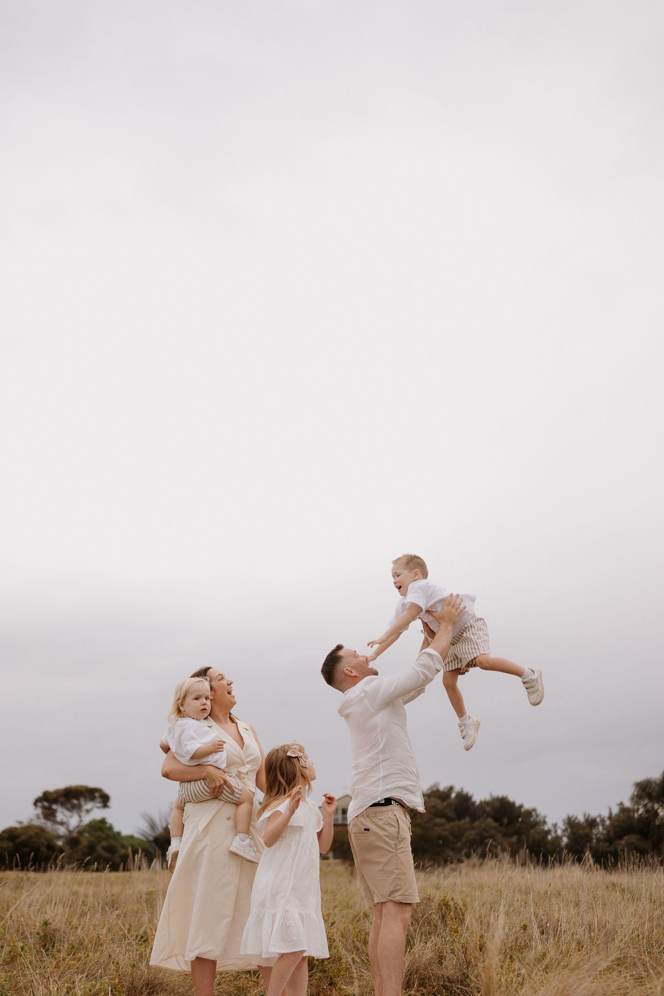 A family playing together in a field near an old barn at sunset.