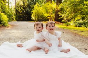Twin babies lying together on white blanket outdoors in natural setting.