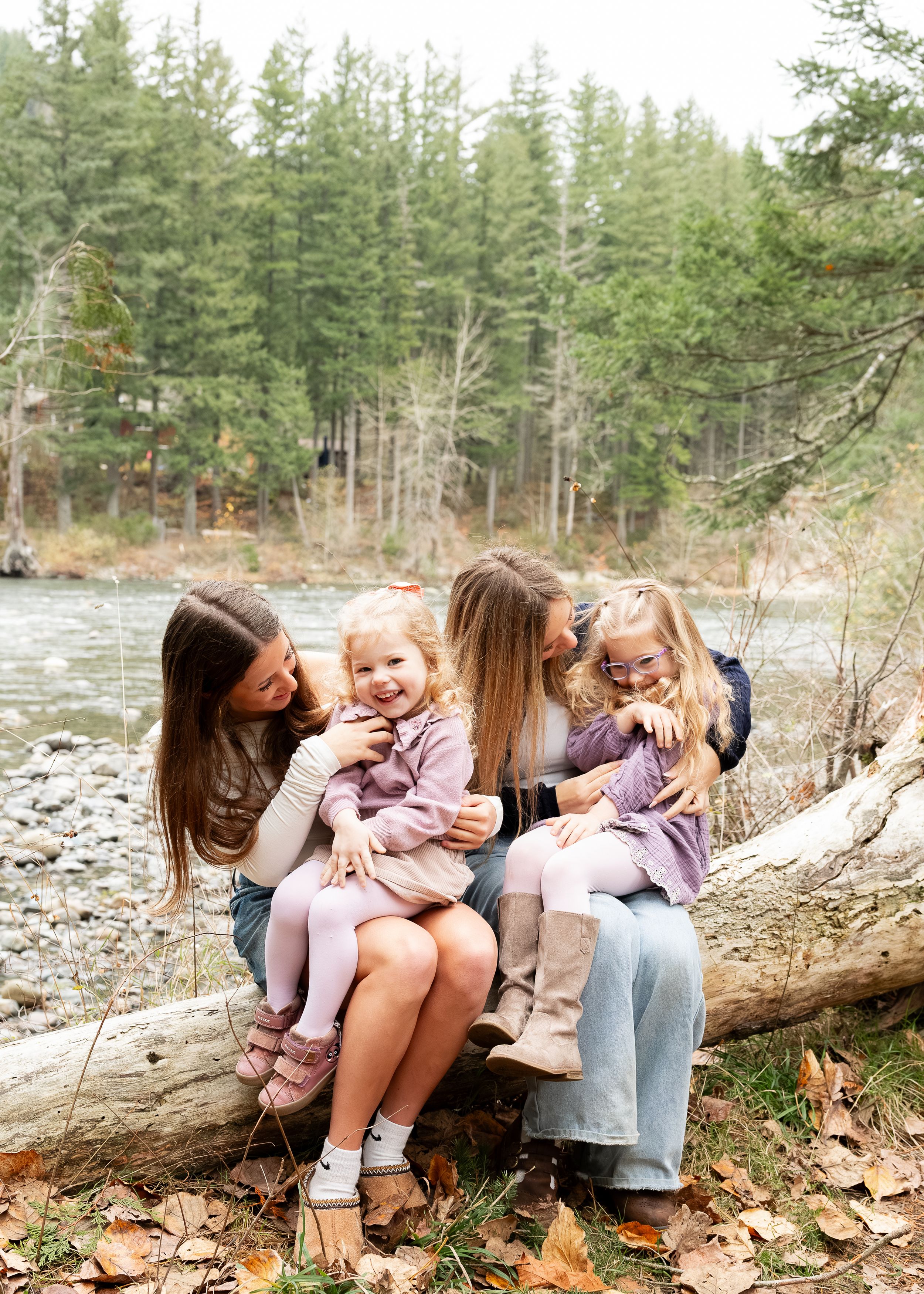 A group sits together on a fallen log in a wooded area near water.