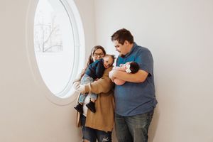 A family shares a tender moment near a round window in a bright room.