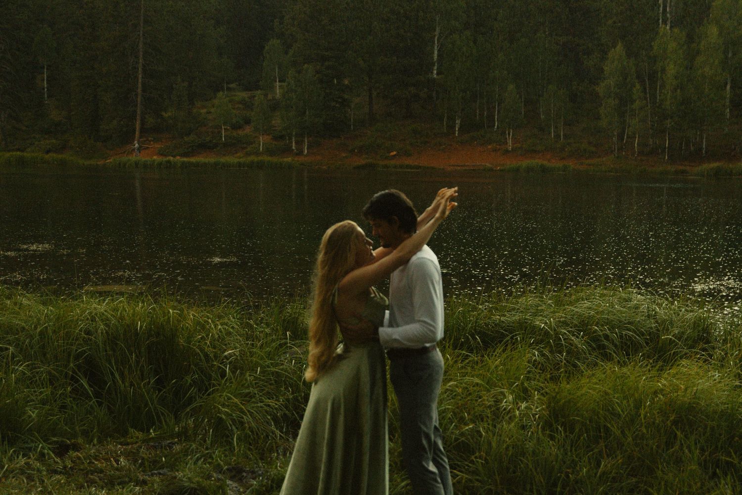Vast grassy mountainous landscape at sunset with a couple in the center, hugging and enjoying a romantic moment together.
