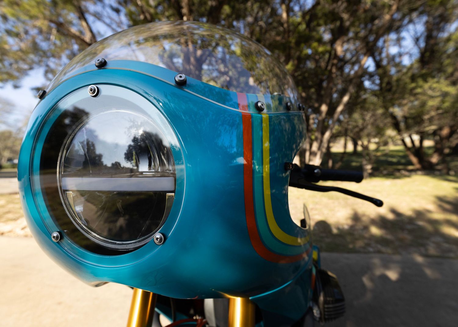 Close-up of turquoise motorcycle headlight featuring retro rainbow racing stripes.