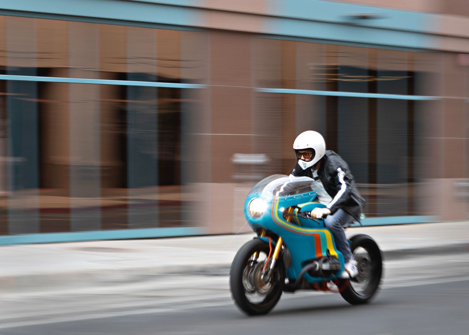 Racing motorcycle with turquoise paint job speeds through city street with motion blur effect.