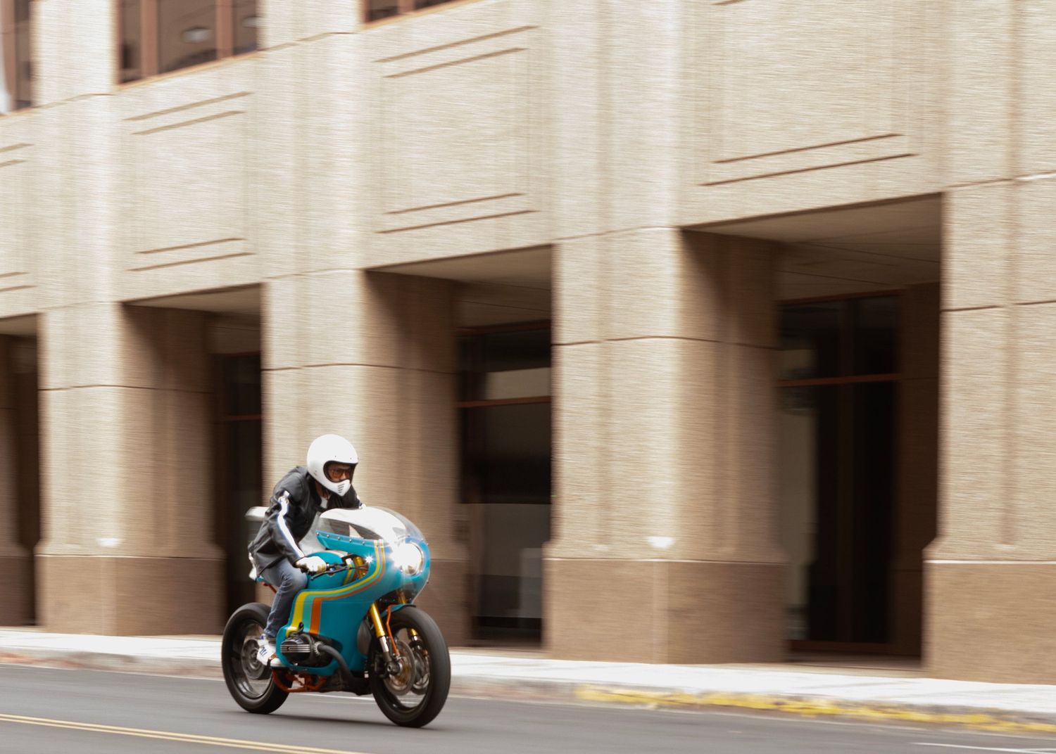 Blue and yellow motorcycle speeds past a beige building facade.