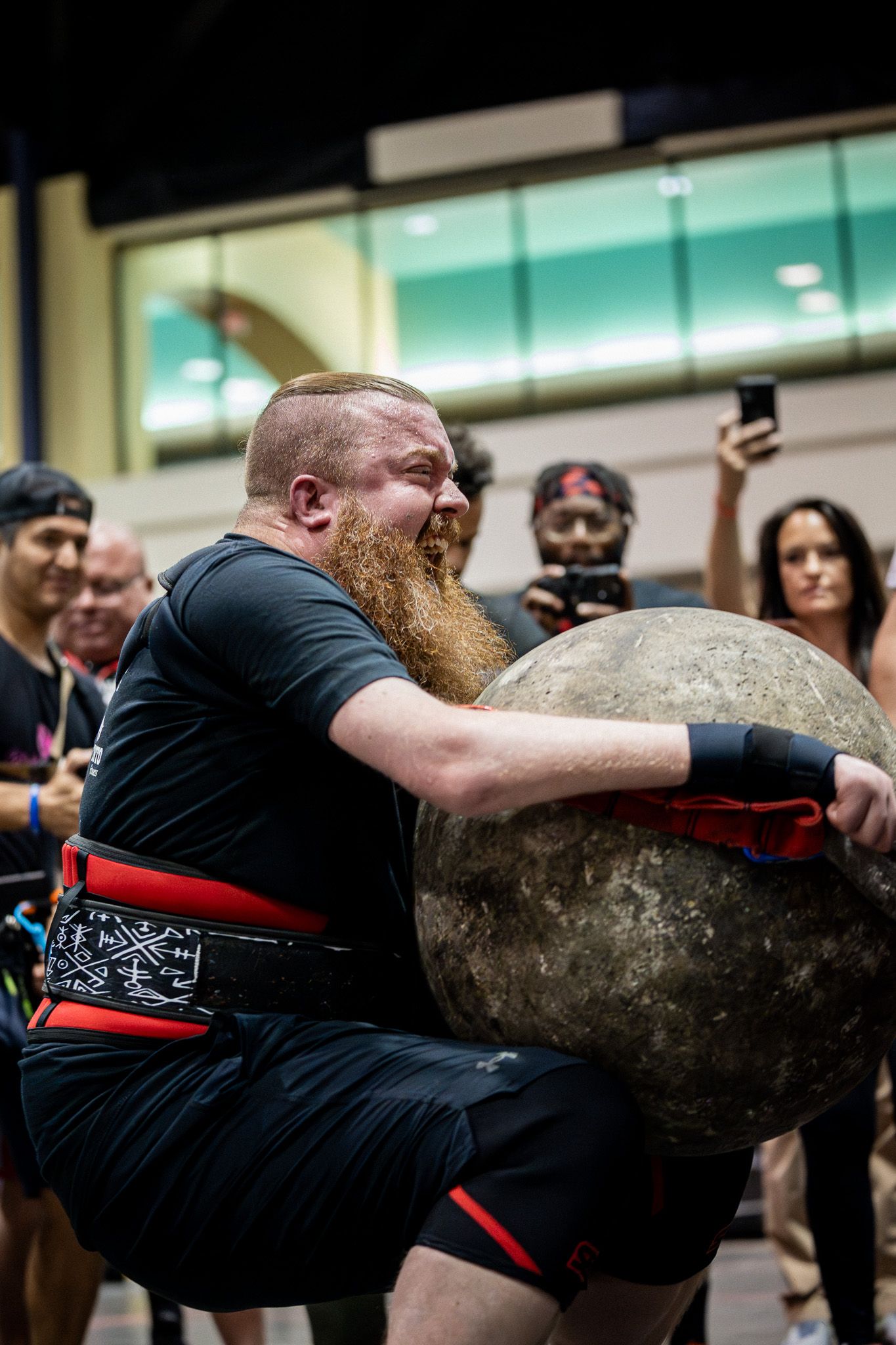 A strongman competitor lifts a heavy Atlas stone during a competition event.