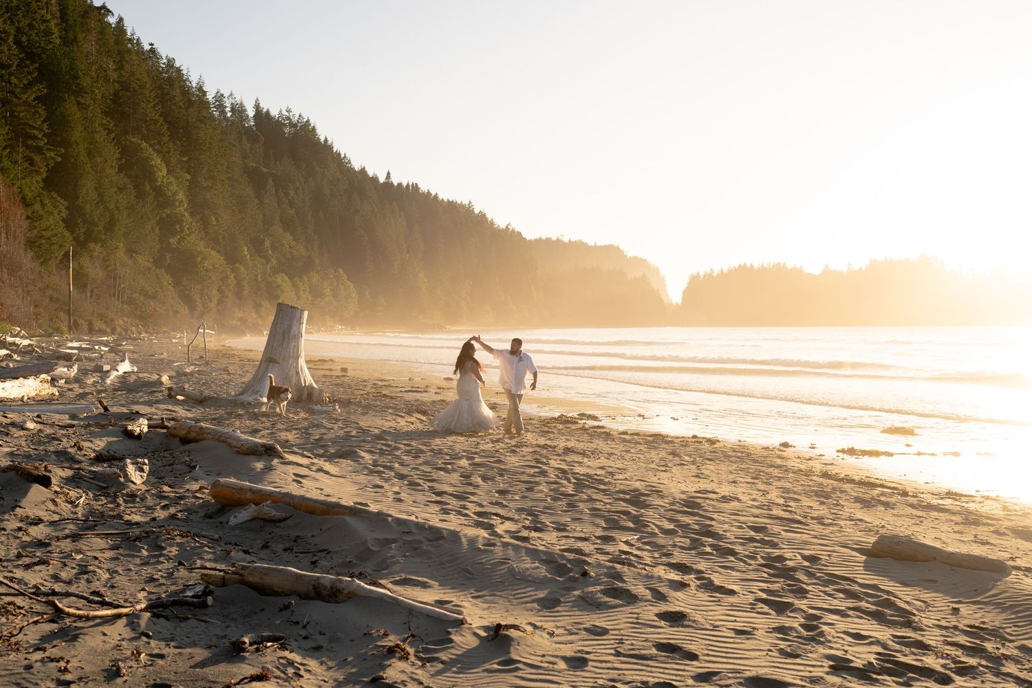 Couple walking along dramatic coastline beach at sunset with cliffs in background.