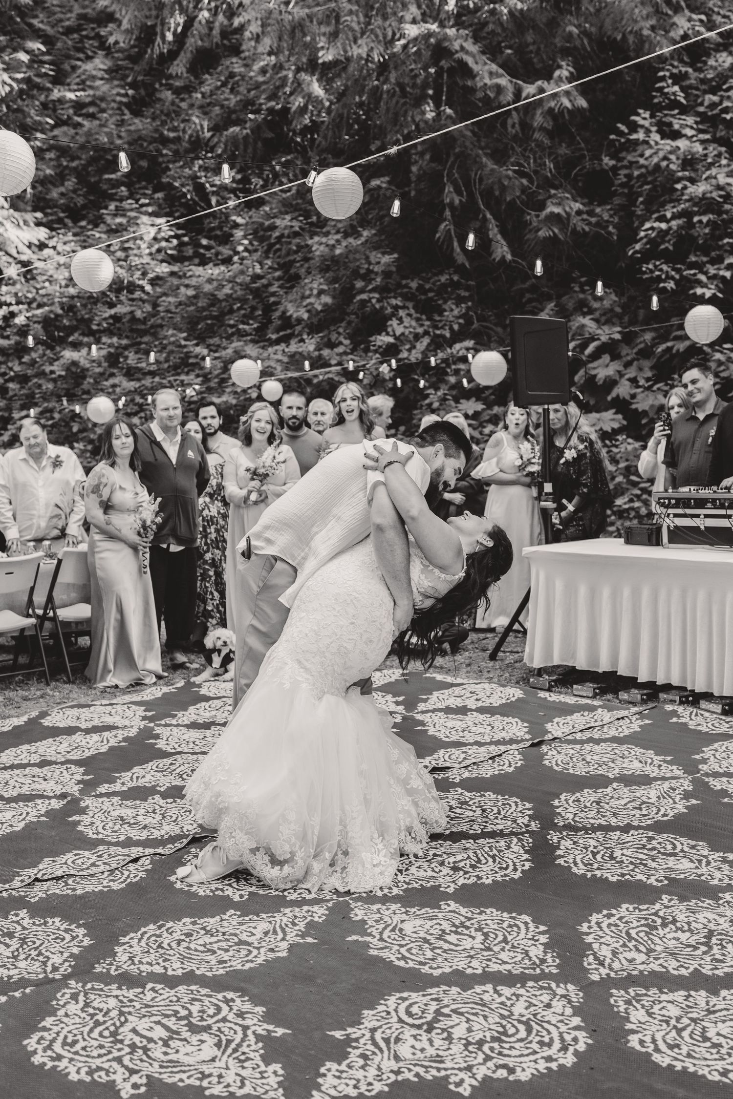 Wedding dance on patterned outdoor dance floor under hanging lanterns in black and white.