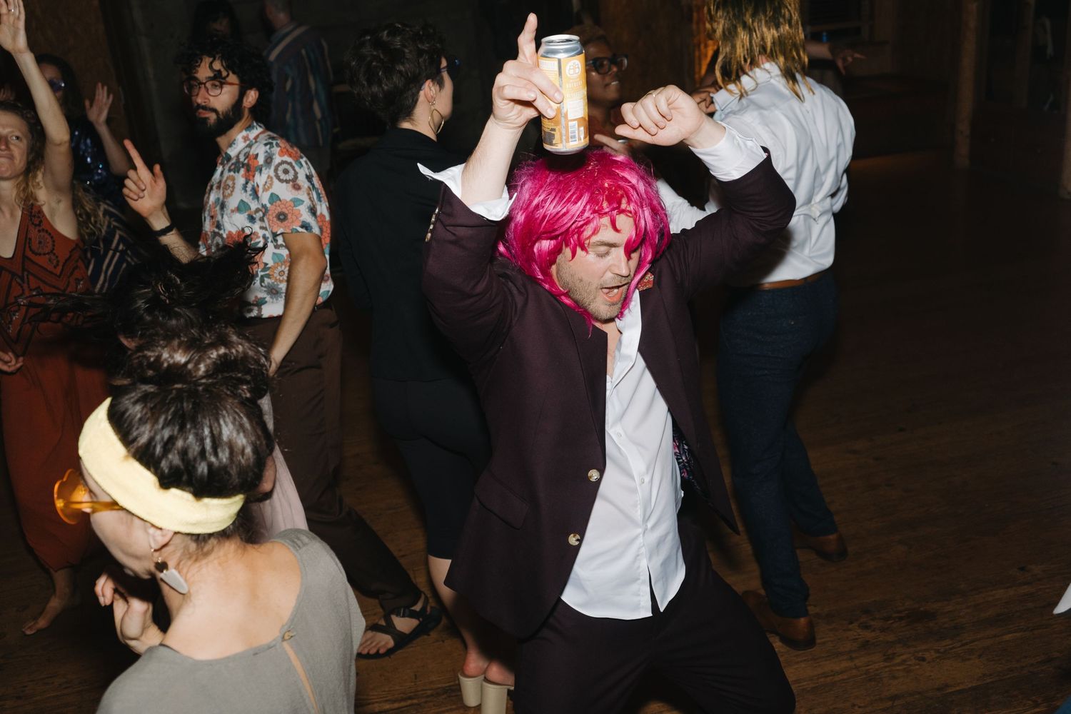 People dancing energetically at a party with someone in a pink dyed hair and white shirt in focus.