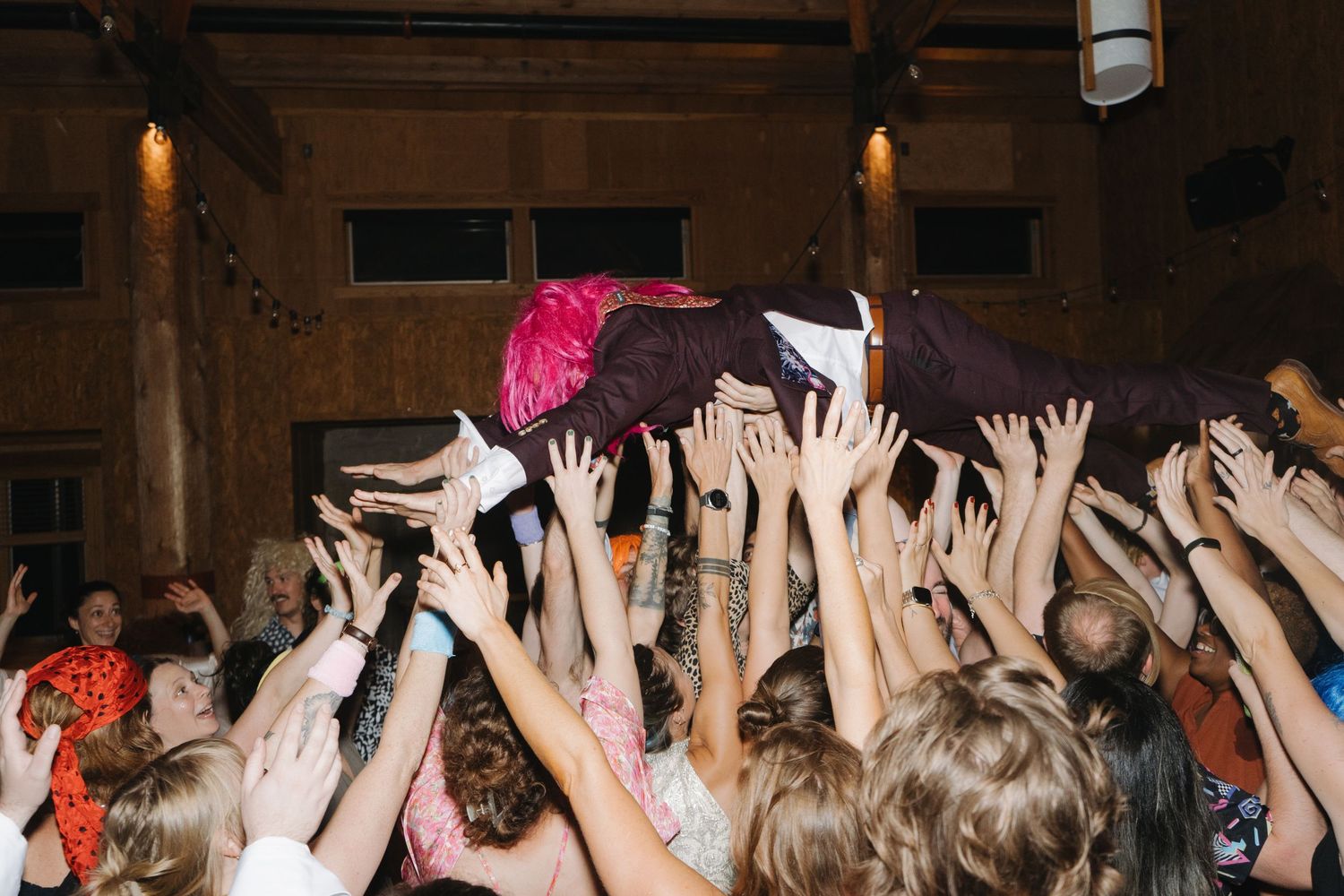 A crowd of raised hands reaches upwards at a concert venue with moody lighting.