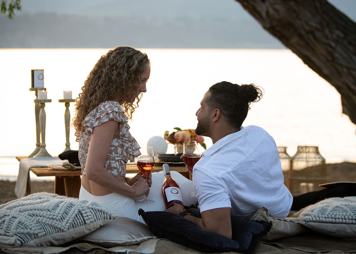 Couple in neutral tones enjoying luxury picnic with Phantom Creek Estates rose on beach by lake - Okanagan lifestyle branding photo.