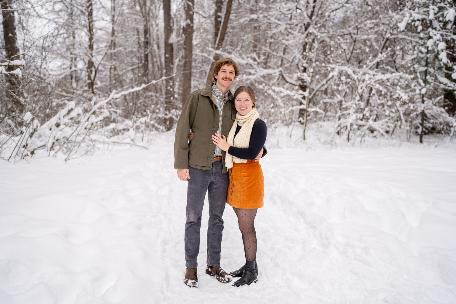 A couple stands in a snowy winter forest during a romantic photo shoot.