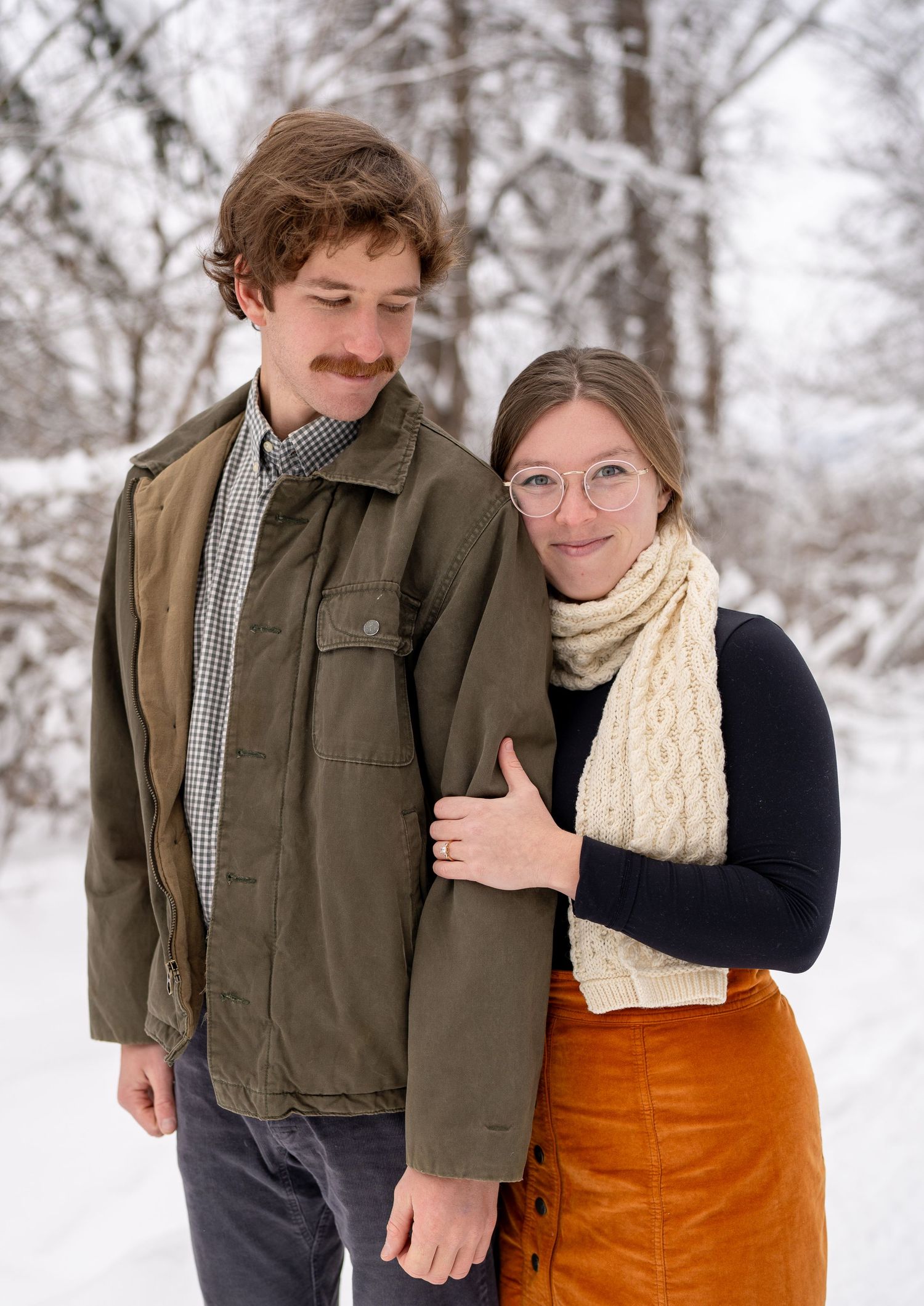 A couple shares an intimate winter moment outdoors in the snow, wearing warm clothing and smiling together.