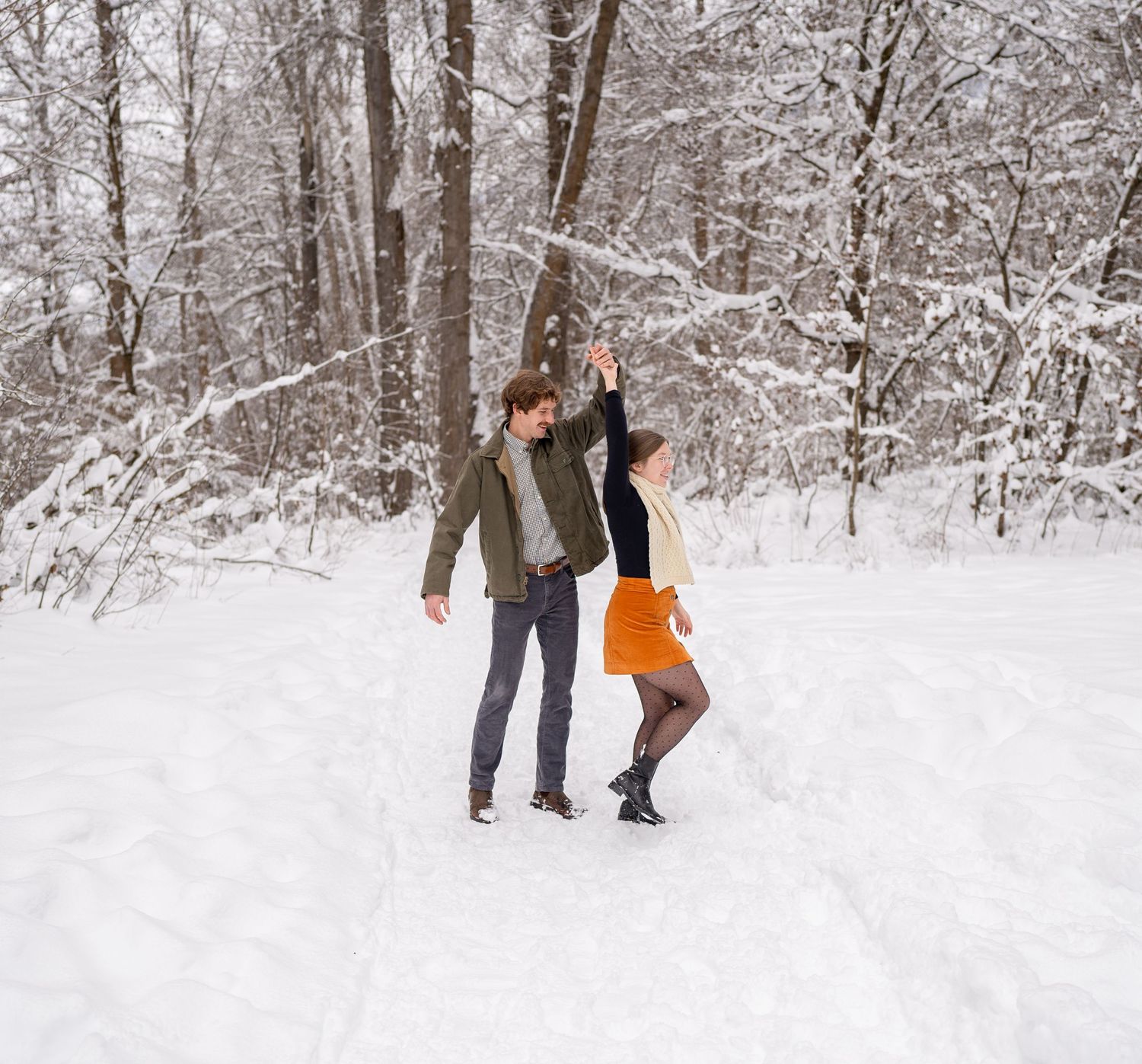 Two people playing and dancing together in snowy winter forest setting with one wearing orange dress.