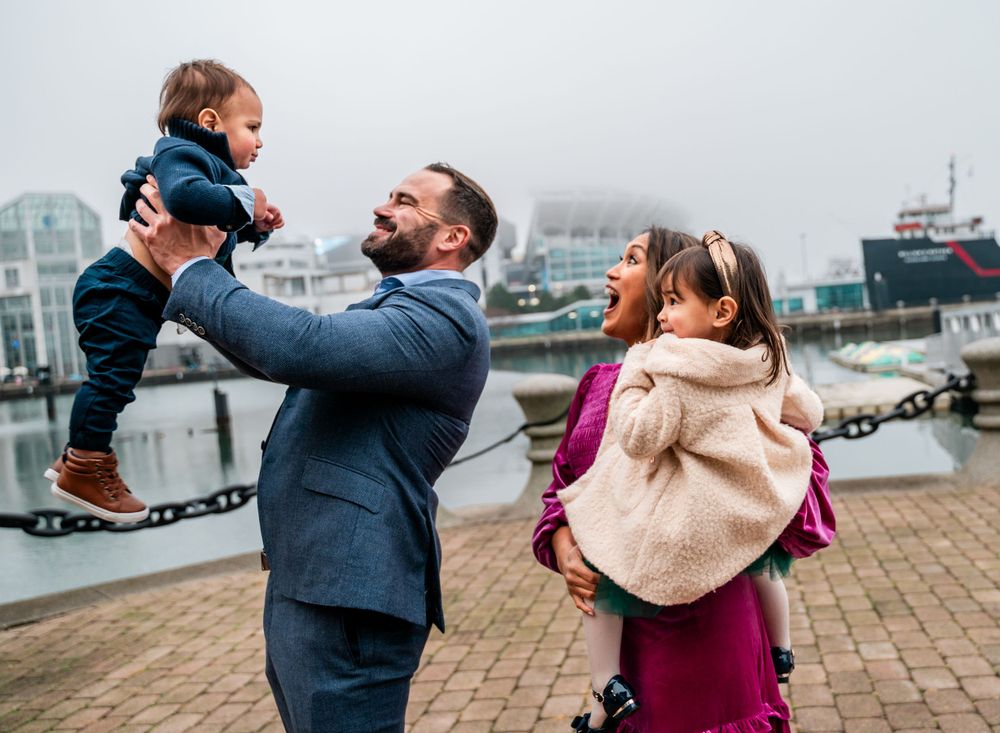 A happy family moment captured by the water with boats in the background.