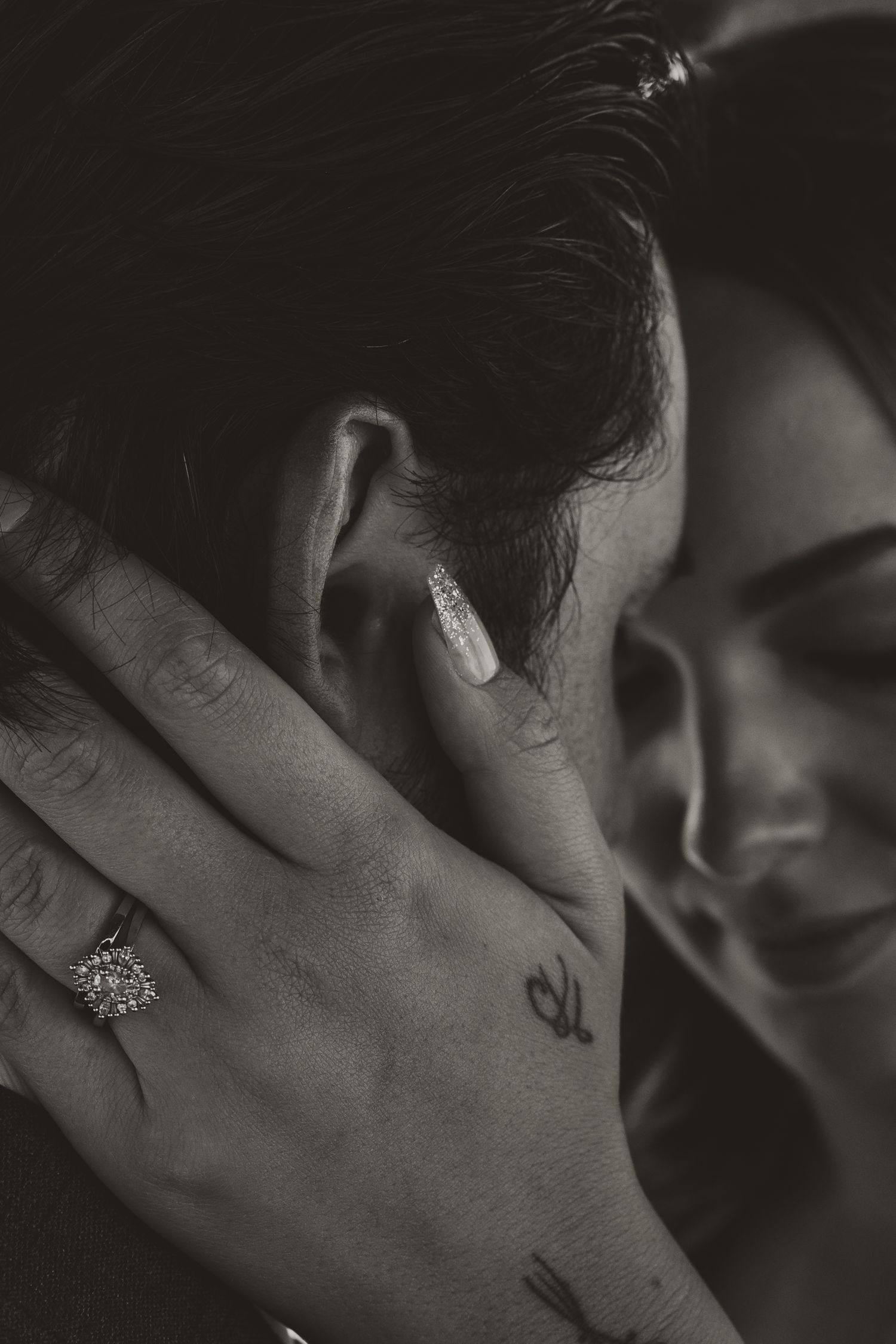 Intimate black and white portrait showing hand with engagement ring and delicate embrace.