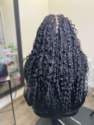 Long black curly hair with defined spiral patterns shown from behind on a salon chair.