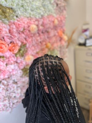 Detailed view of neatly braided black box braids against a pink floral backdrop in a salon setting.