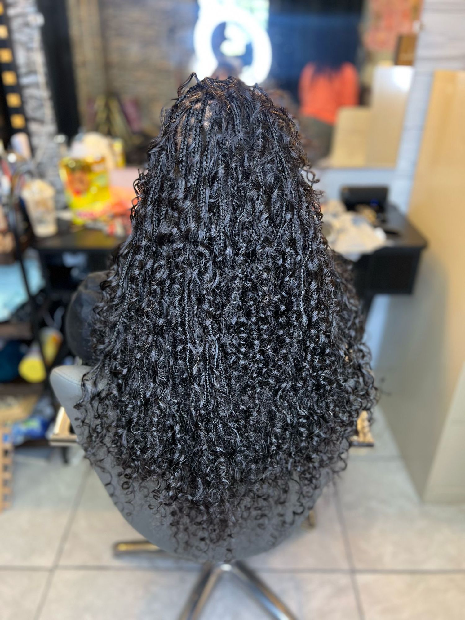 Curly black textured hair styled in natural long ringlets is shown from behind in a salon chair.