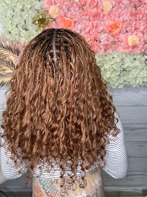 Back view of long brunette curly hair styled in micro braids against floral backdrop with pink and white flowers.