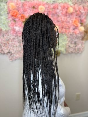 Long black box braids styled in a straight pattern against a backdrop of pink floral decorations.