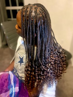 Long black box braids styled with curled ends cascade down against a Dallas Cowboys shirt in a detailed hair styling photo.