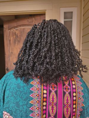 Back view of a person wearing a teal and pink patterned dress with detailed natural black curly hair.
