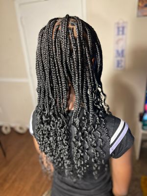 A back view of dark box braids with curled ends styled in a casual manner against a light background.