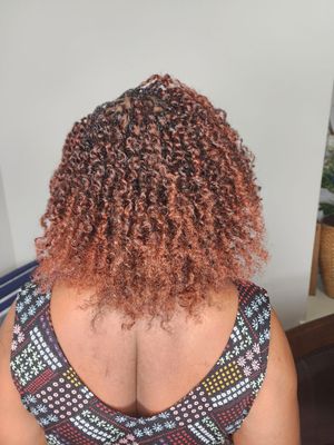 Back view of curly dyed reddish-pink hair styled in a natural pattern against light background.