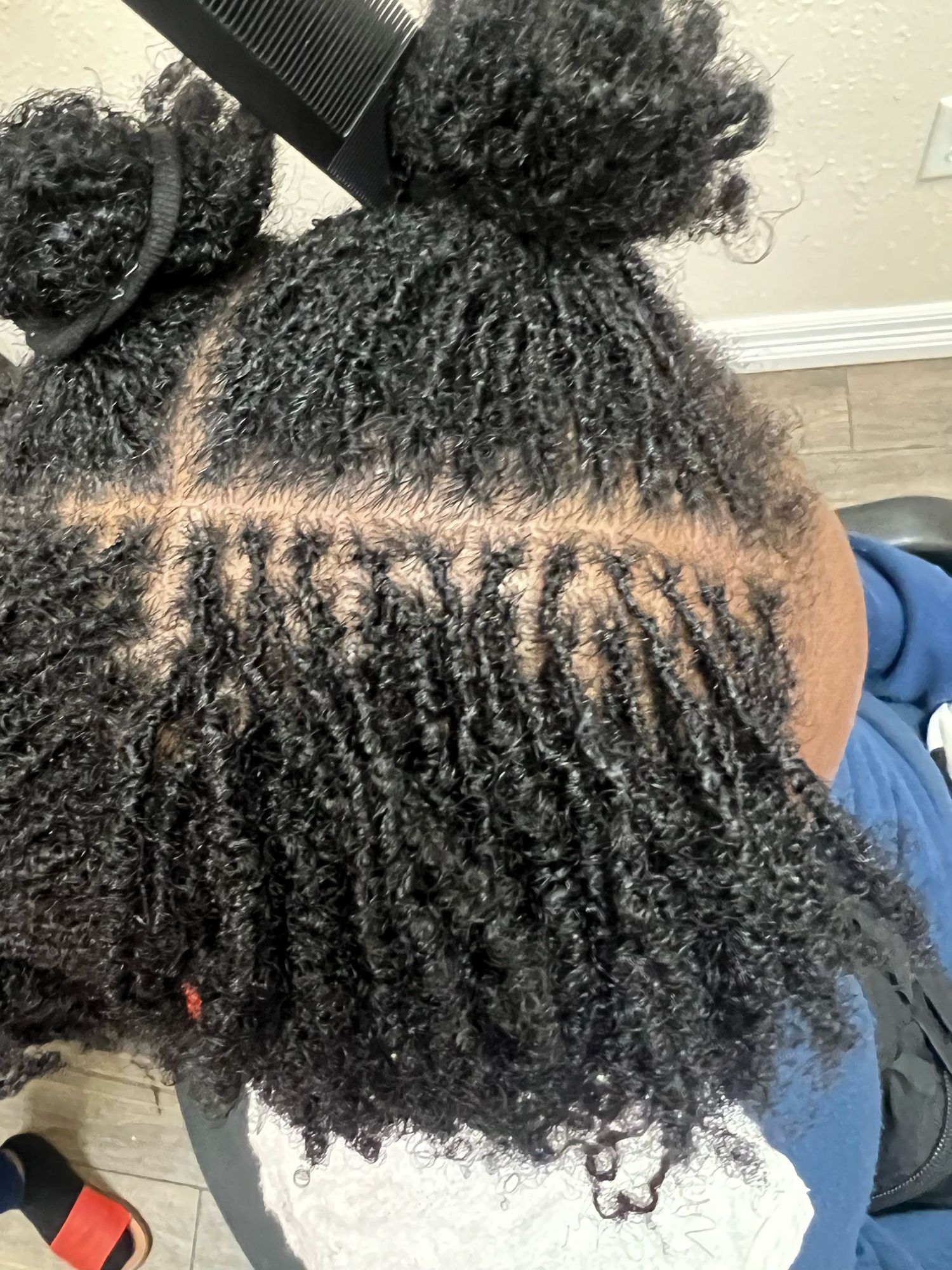 Close-up view of natural curly hair styled in cornrow braids with two bun sections and kinky coily texture.