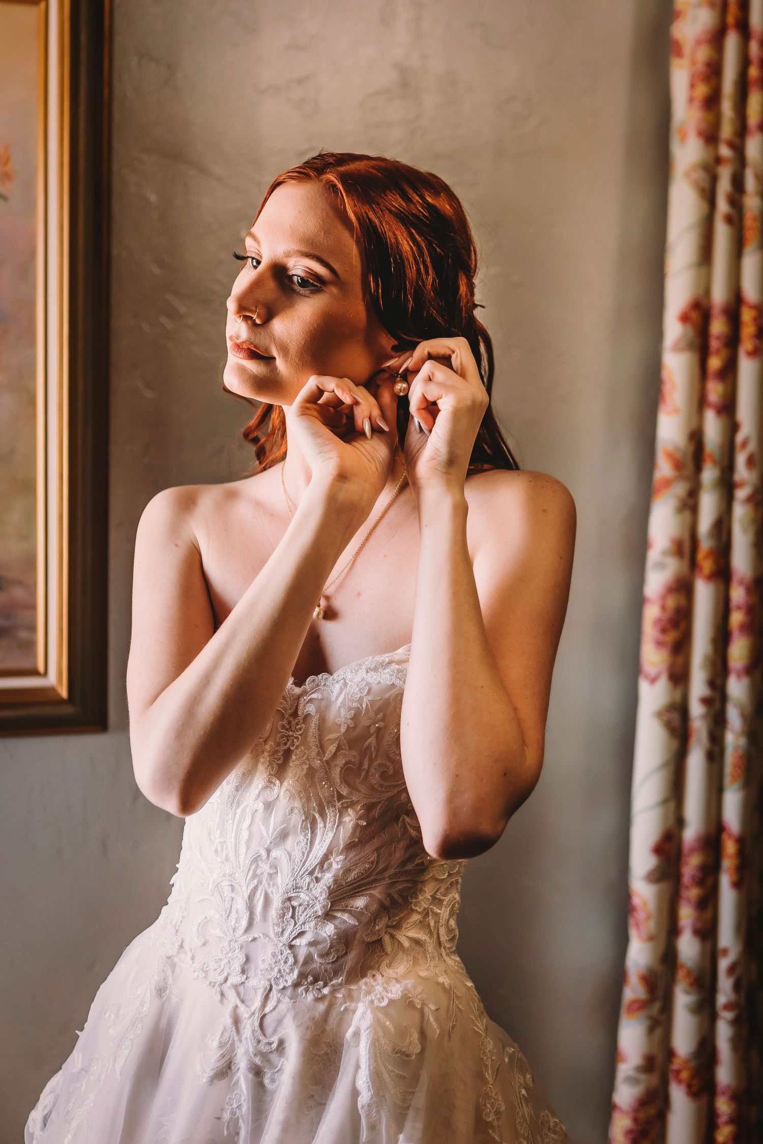 Person in a white lace wedding dress adjusting earrings while getting ready.