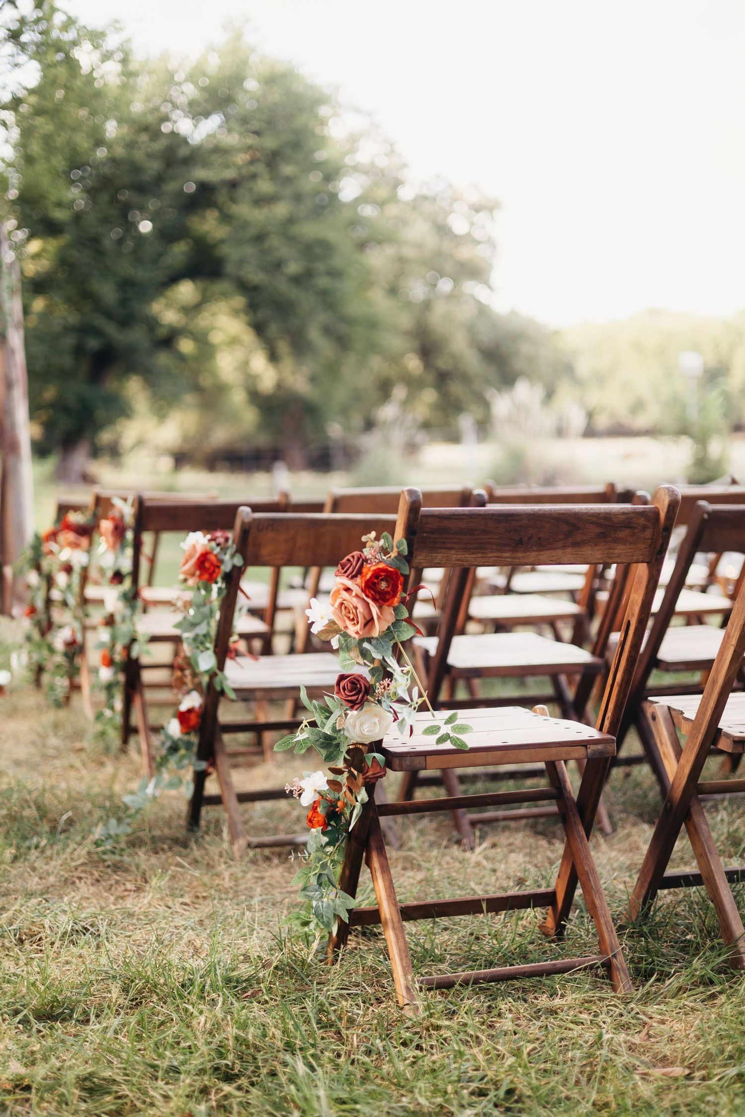 Wooden folding chairs decorated with floral arrangements set up for an outdoor wedding ceremony.