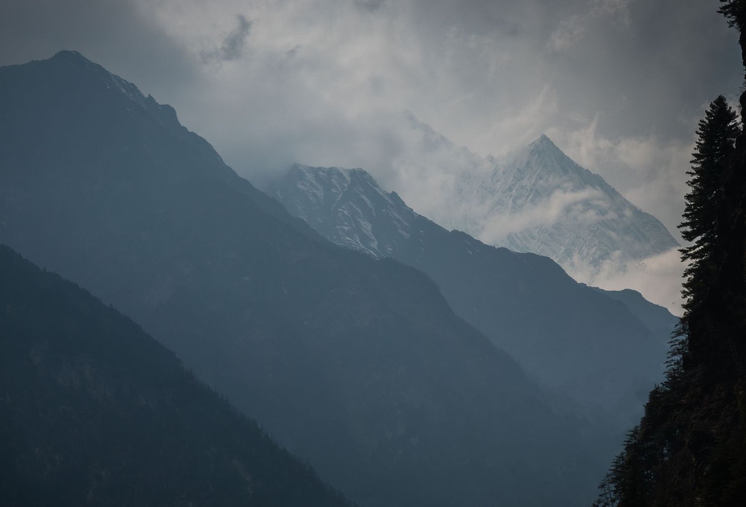Layered mountain peaks fade into misty distance under dramatic cloudy skies.