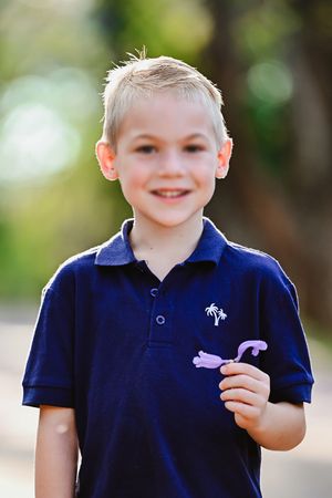 A picture of a young man, smiling at the camera, with a Jakaranda flower in hand.