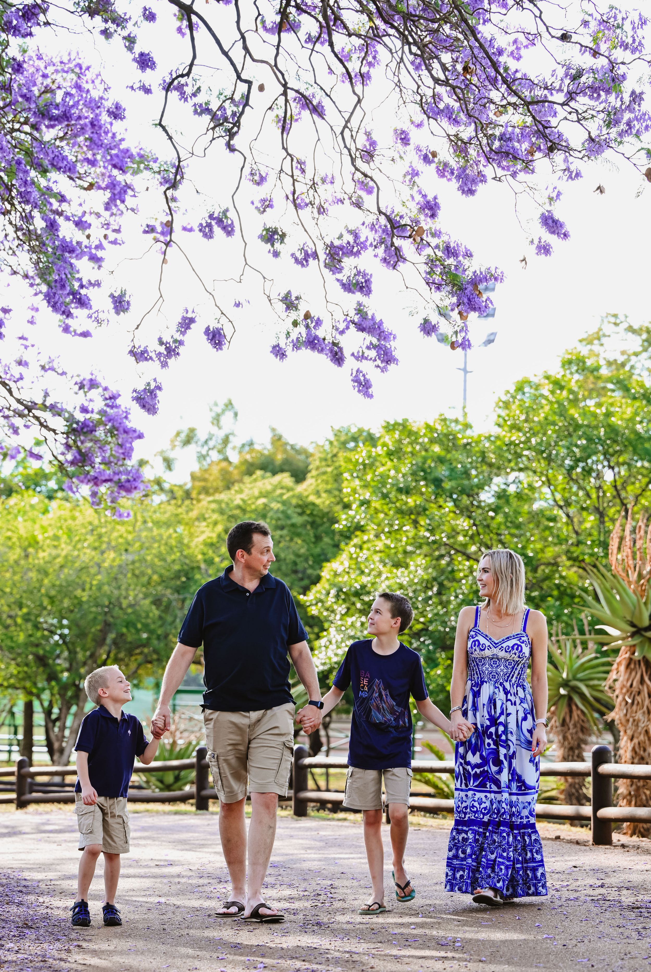 Family enjoying a walk beneath purple Jacaranda blossoms during a Pretoria photo-shoot.