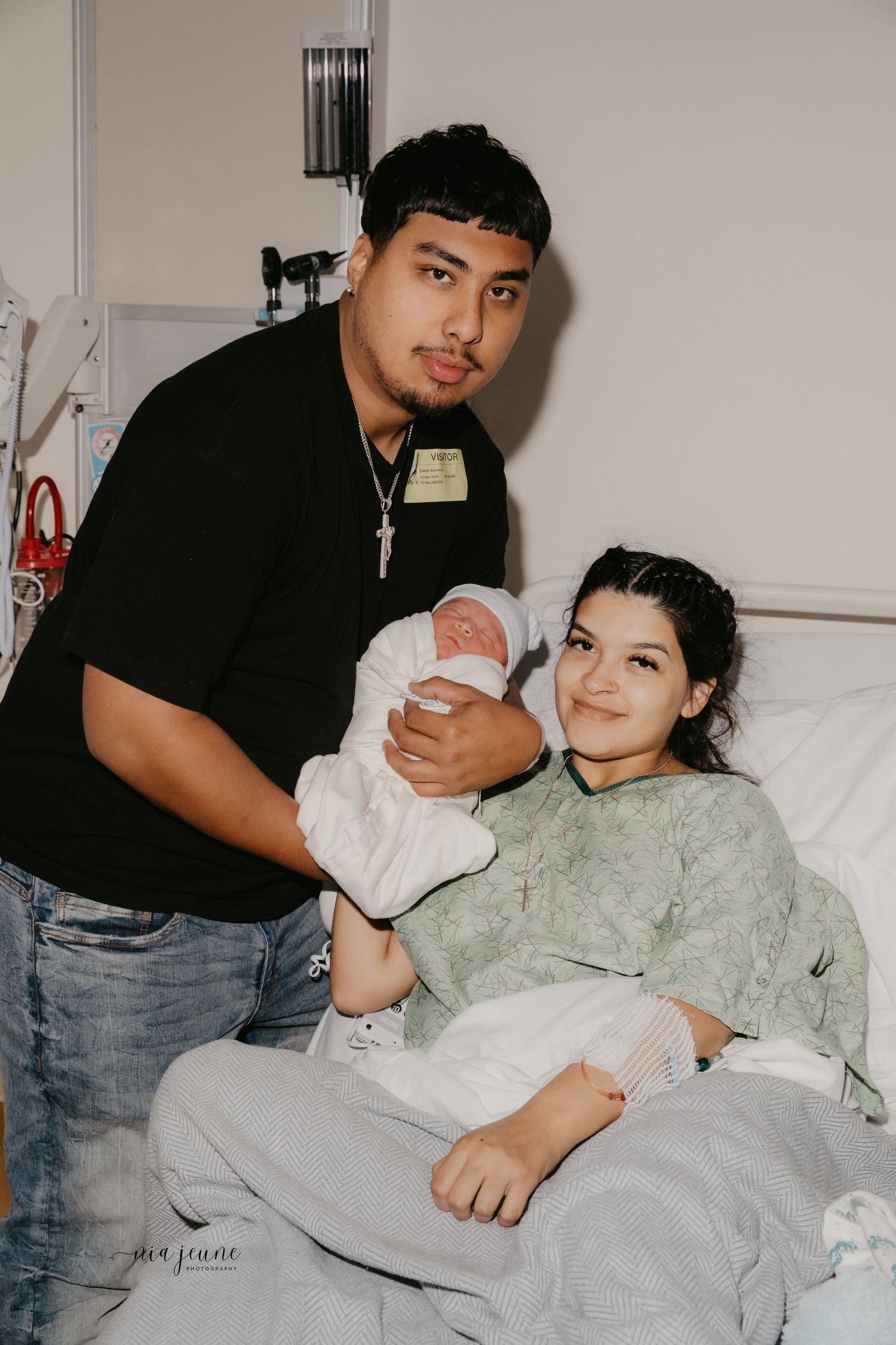 Proud new parents with baby in hospital room after birth.