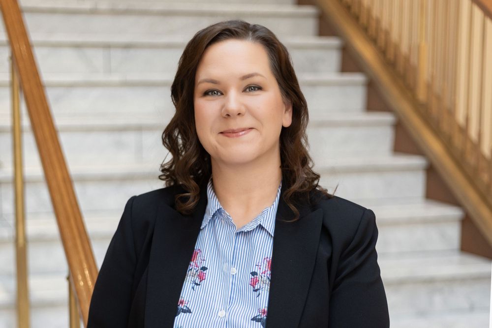 Professional headshot of person in business attire against staircase background.