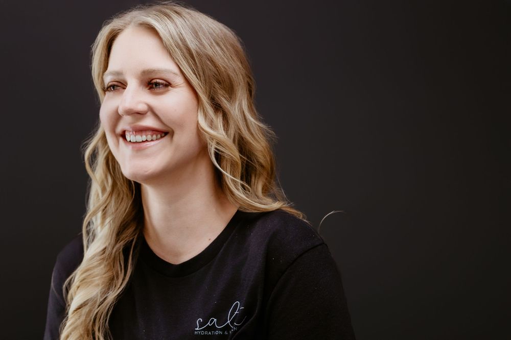 Smiling blonde woman in black t-shirt against dark background, professional portrait photo.