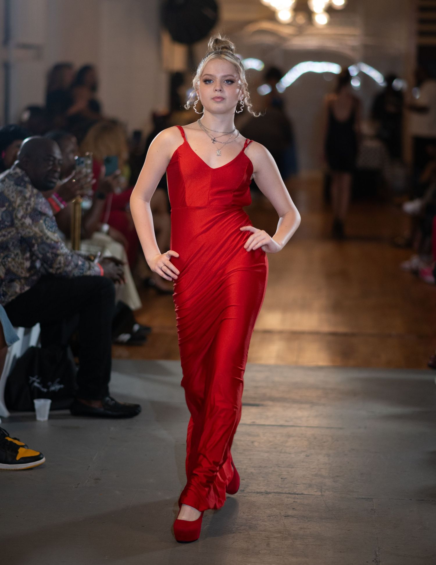 Sleek red satin evening gown with matching shoes on fashion runway.