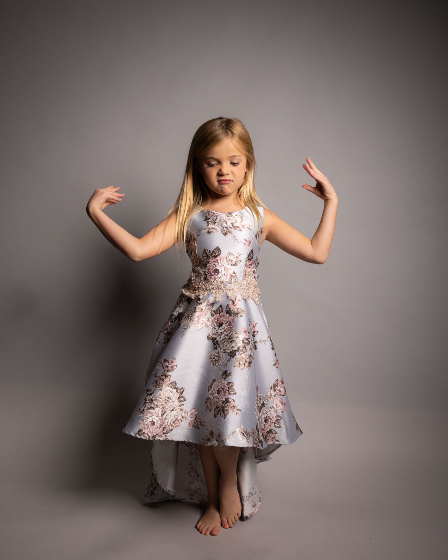 Young dancer in a floral dress twirls on a gray backdrop, barefoot and carefree.